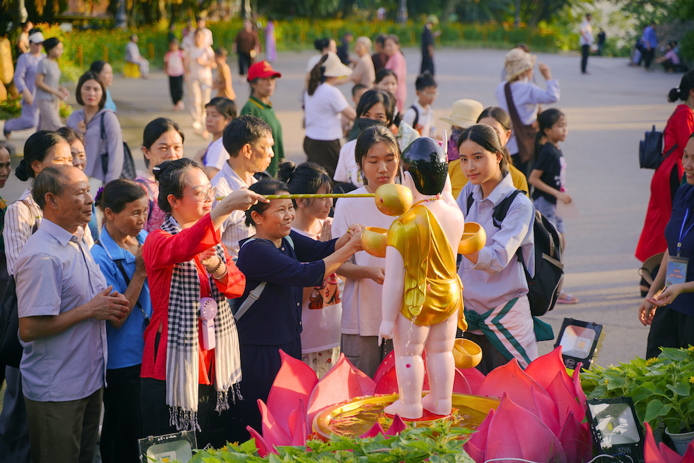 Bạn Trần Ngọc Ánh (mặc áo bà ba đỏ) đang thực hiện nghi lễ tắm Phật