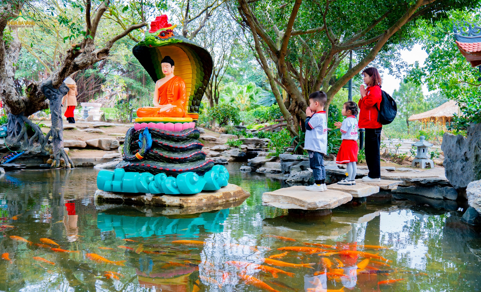 Các bạn nhỏ cùng cô giáo chắp tay kính lễ trước tôn tượng rắn thần che mưa cho Đức Phật  