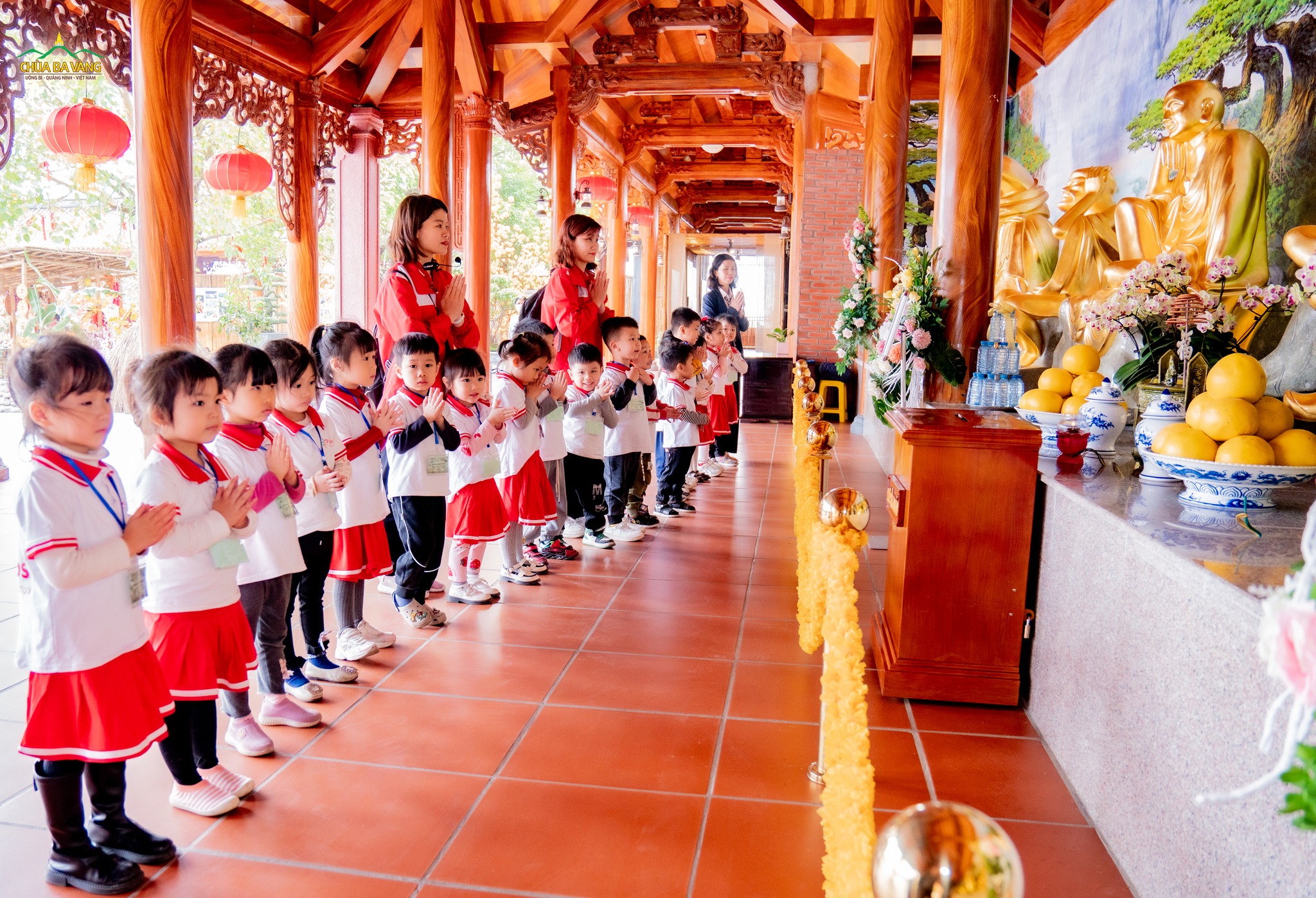 Các bạn nhỏ cùng các cô giáo chắp tay trang nghiêm đối trước tôn tượng các vị A La Hán  